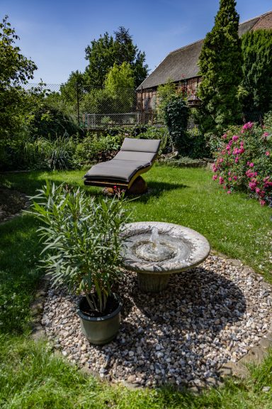 Garten mit Liegestuhl, Wasserbecken und Blumenbeeten im Hintergrund.